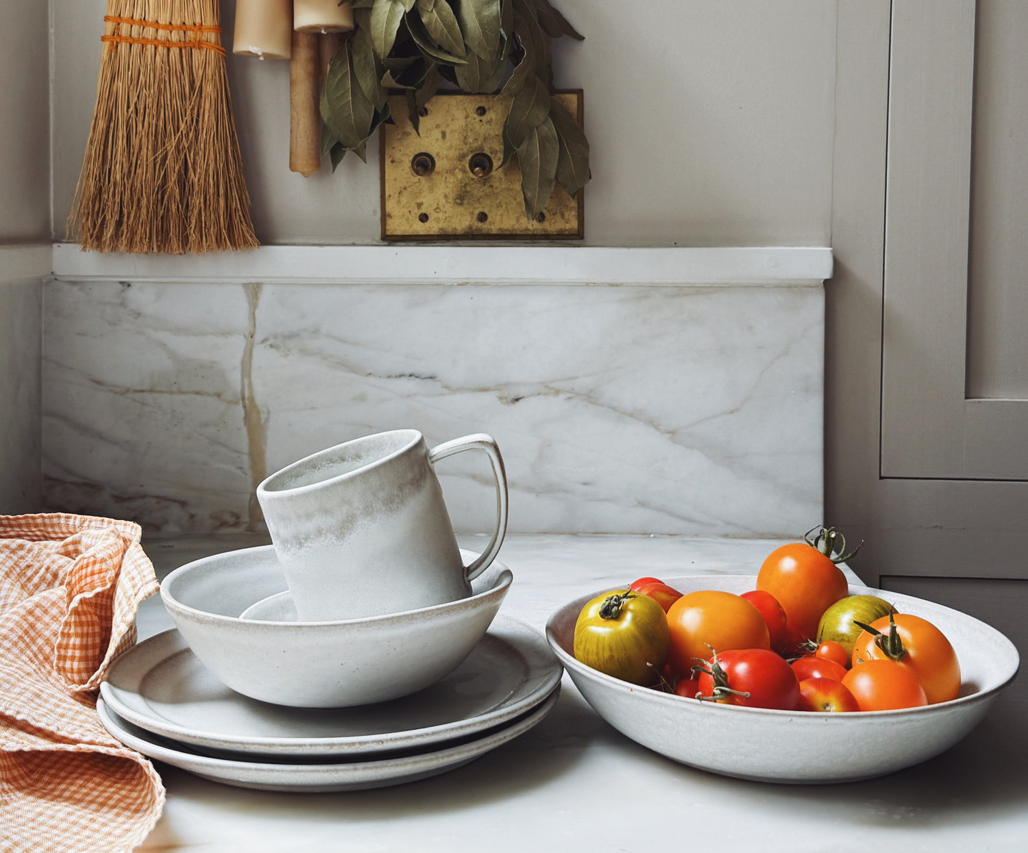 Kitchen counter with white dishes, a bowl of tomatoes, and decorative items on a marble backsplash.