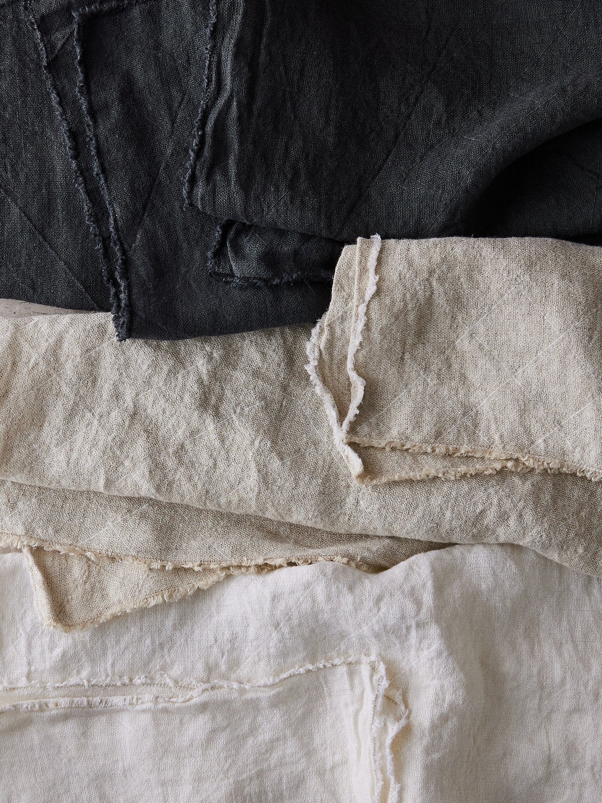 Stack of slate grey, natural, and white fabric pieces with grid jacquard pattern and frayed edges.