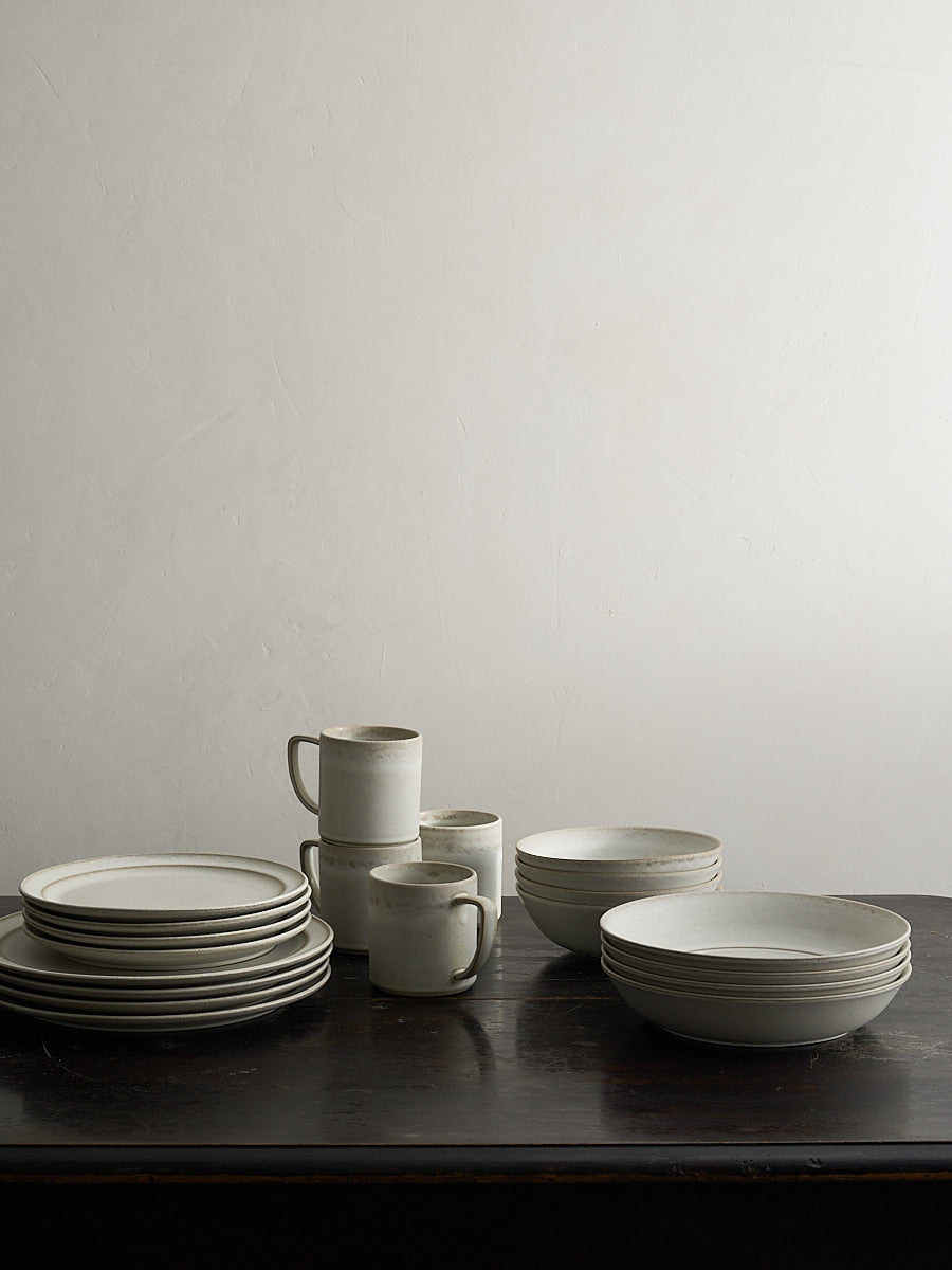 Set of white ceramic dishes on a dark table with a Roman clay background