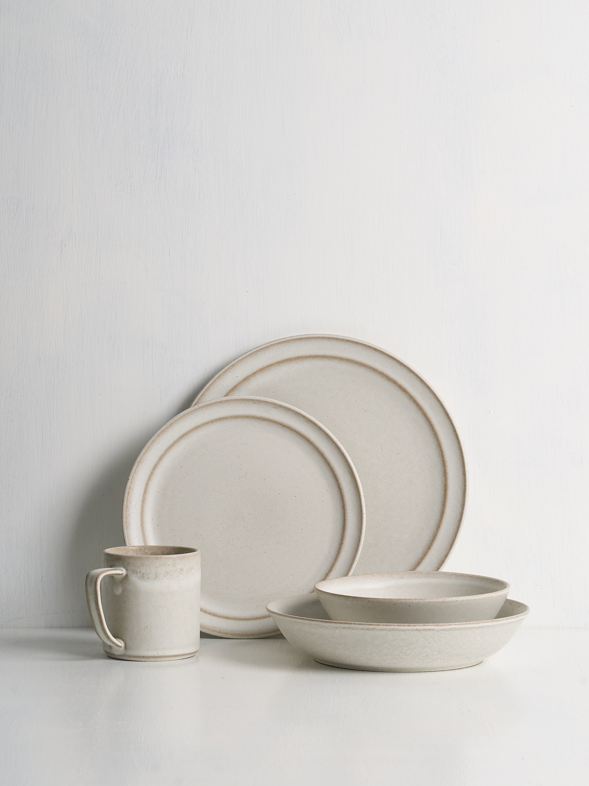 Set of ceramic dinnerware including plates and a mug on a light gray background
