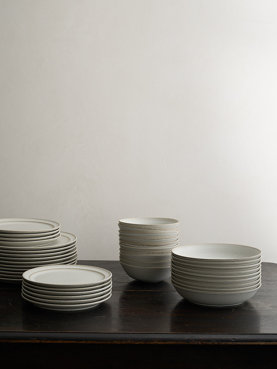 Stacks of white ceramic plates and bowls on a dark surface with a light gray background