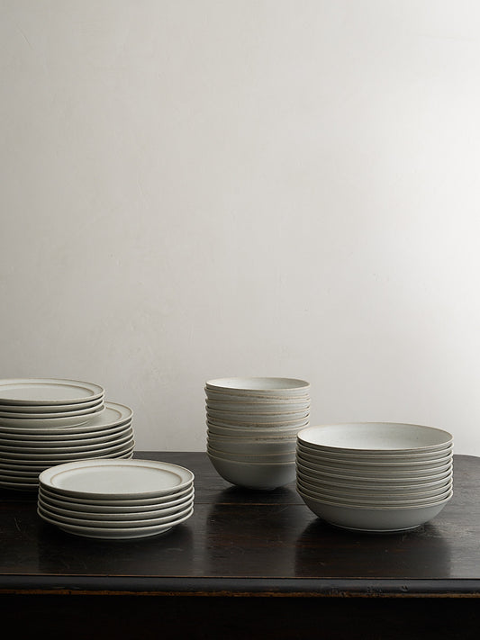 Stacks of white ceramic plates and bowls on a dark surface with a light gray background