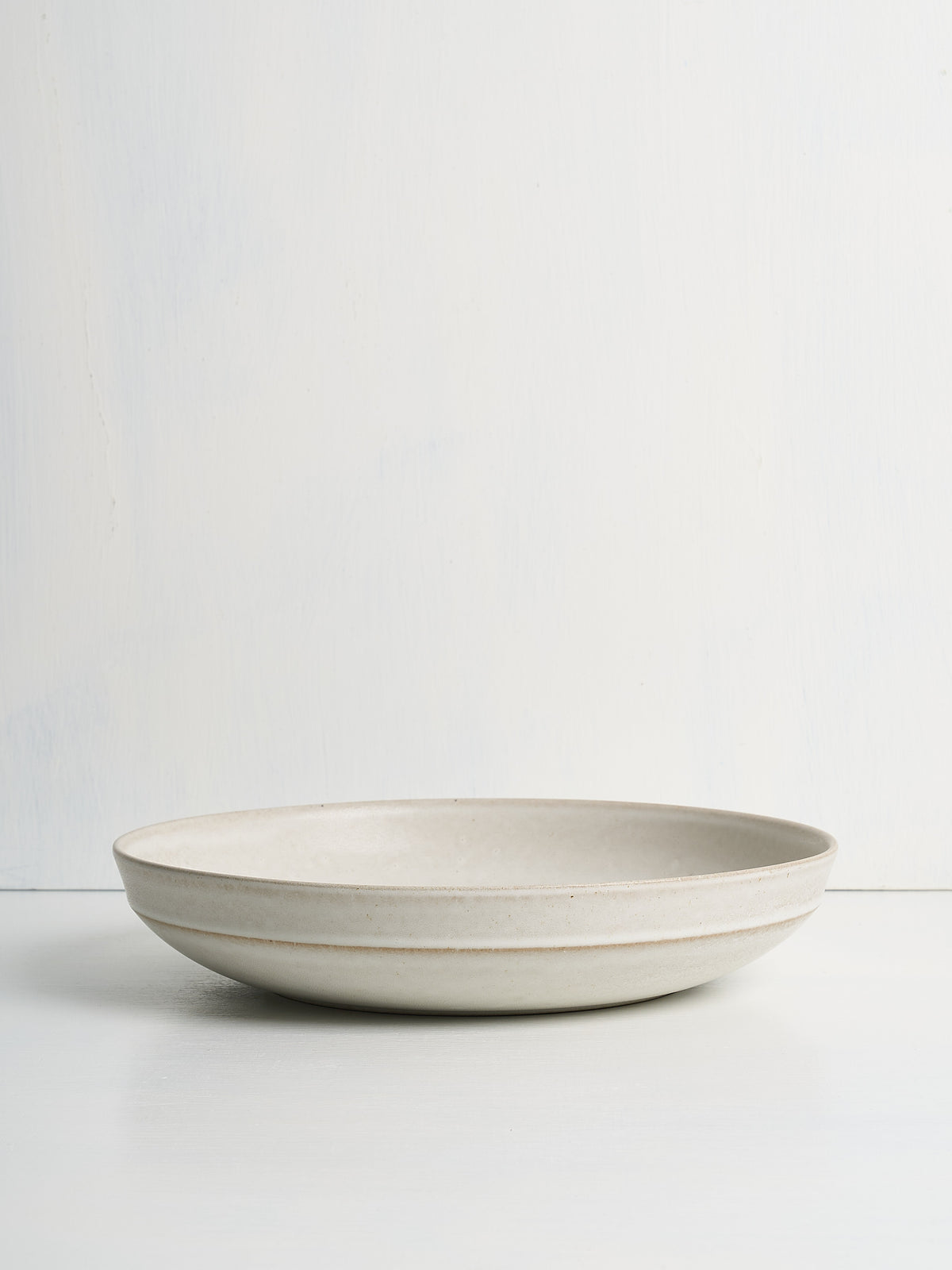 Beige ceramic low serving bowl on a white background