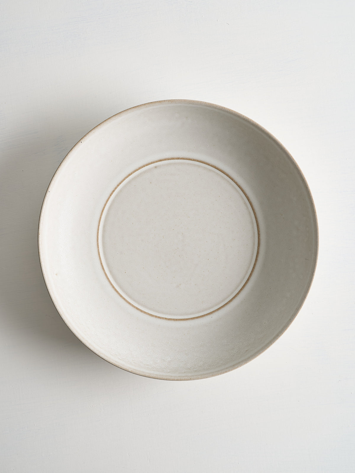 Beige ceramic low serving bowl with brown rim on a white background