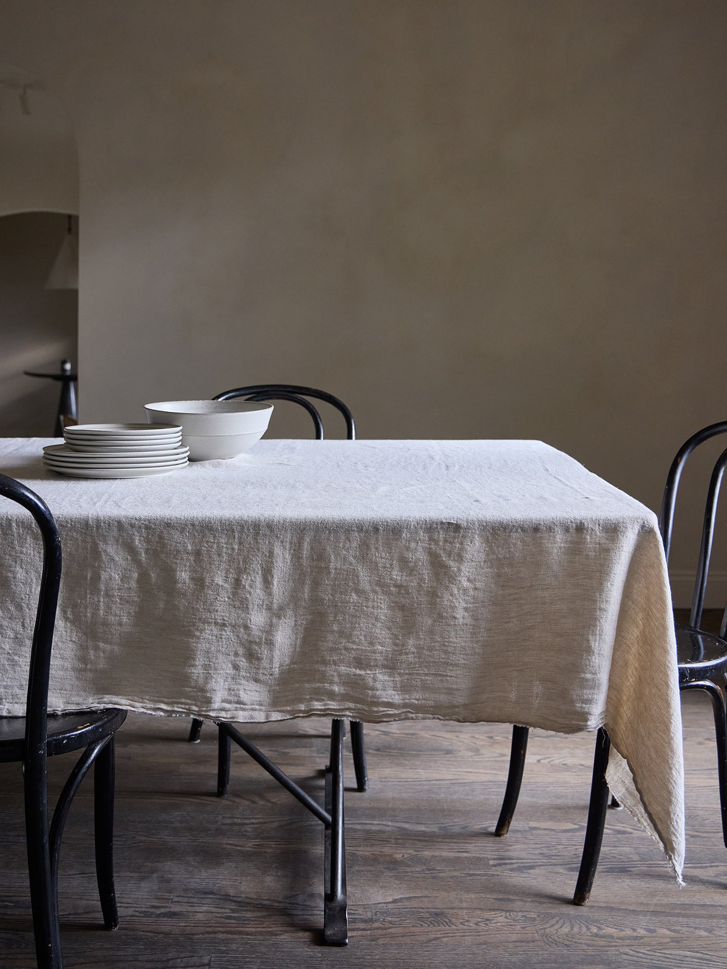 Dining table with a natural tone linen tablecloth and black chairs against a Roman clay wall.