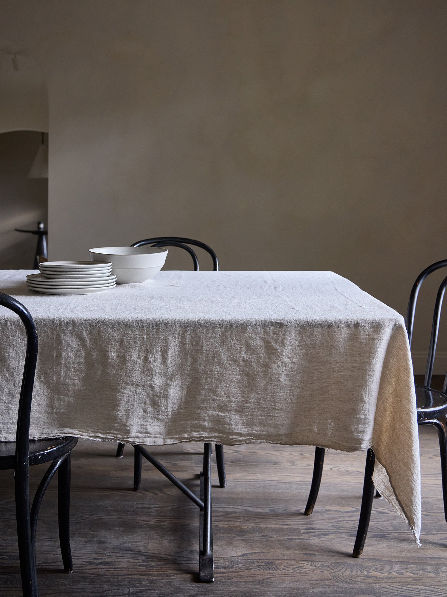 Dining table with a natural tone linen tablecloth and black chairs against a Roman clay wall.