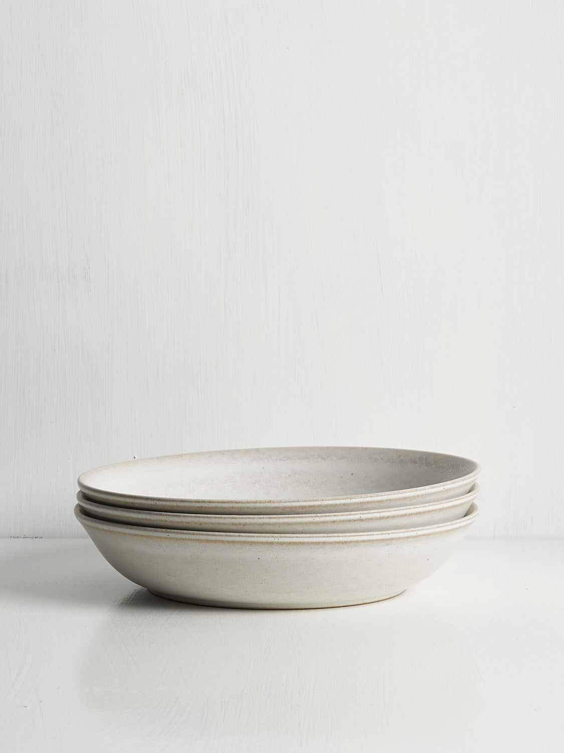 A stack of low-profile white stoneware bowls designed for pasta, grains, or stews