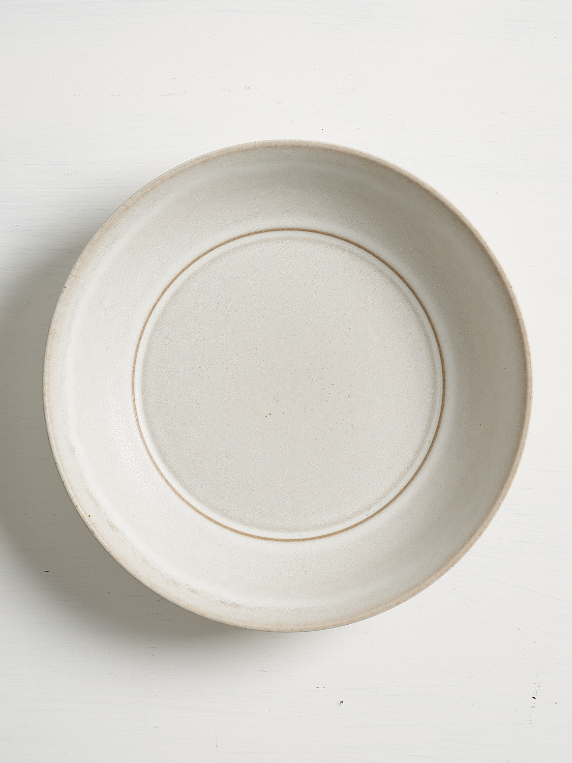 A low, wide white ceramic entree bowl embodying relaxed elegance and timeless design on white background