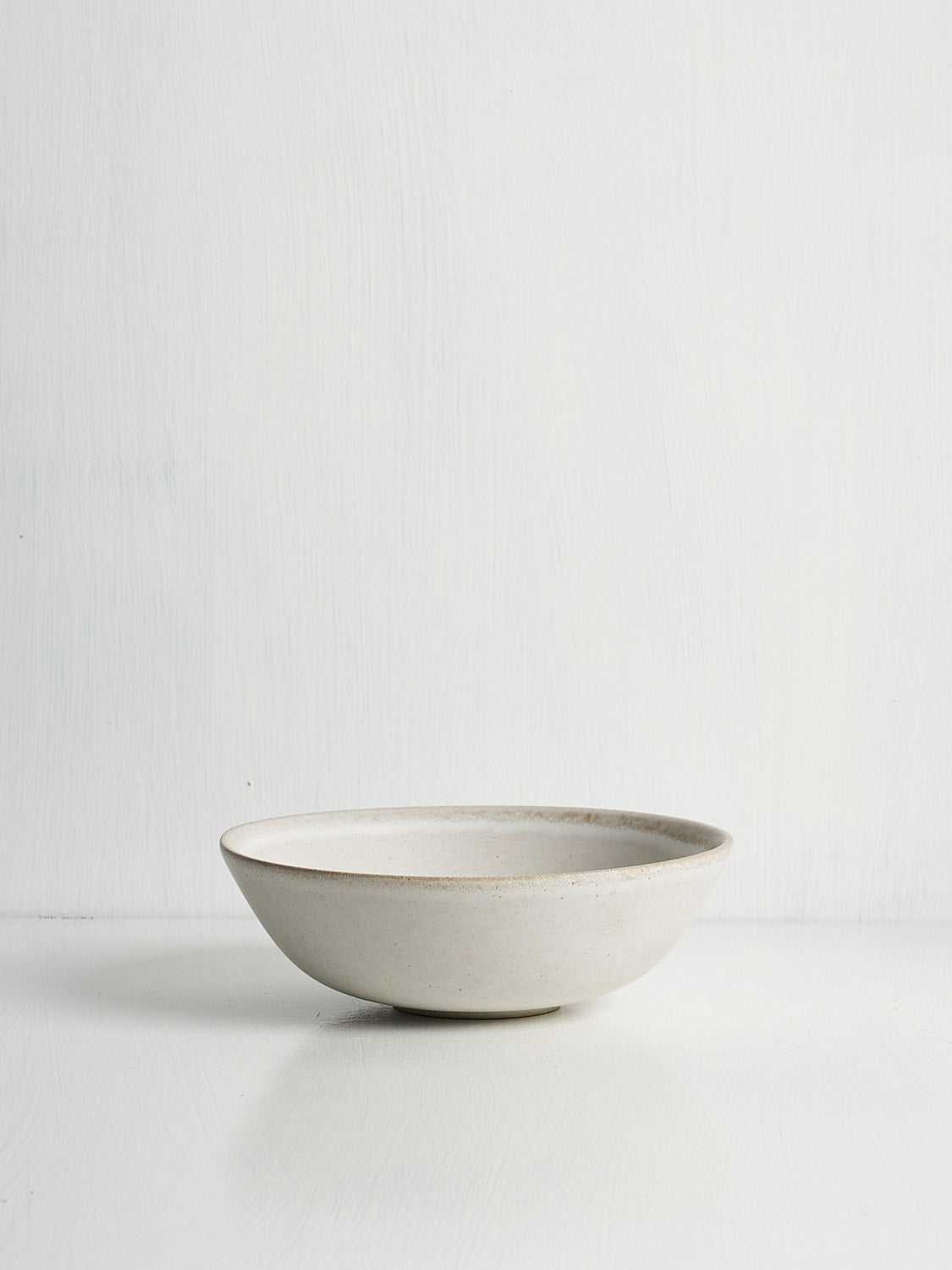 A white ceramic low small bowl with an open curve, displayed against a white background.