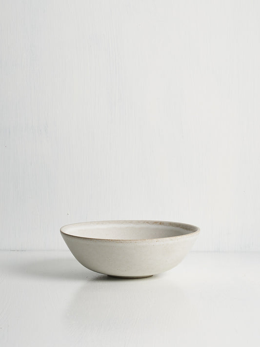 A white ceramic low small bowl with an open curve, displayed against a white background.