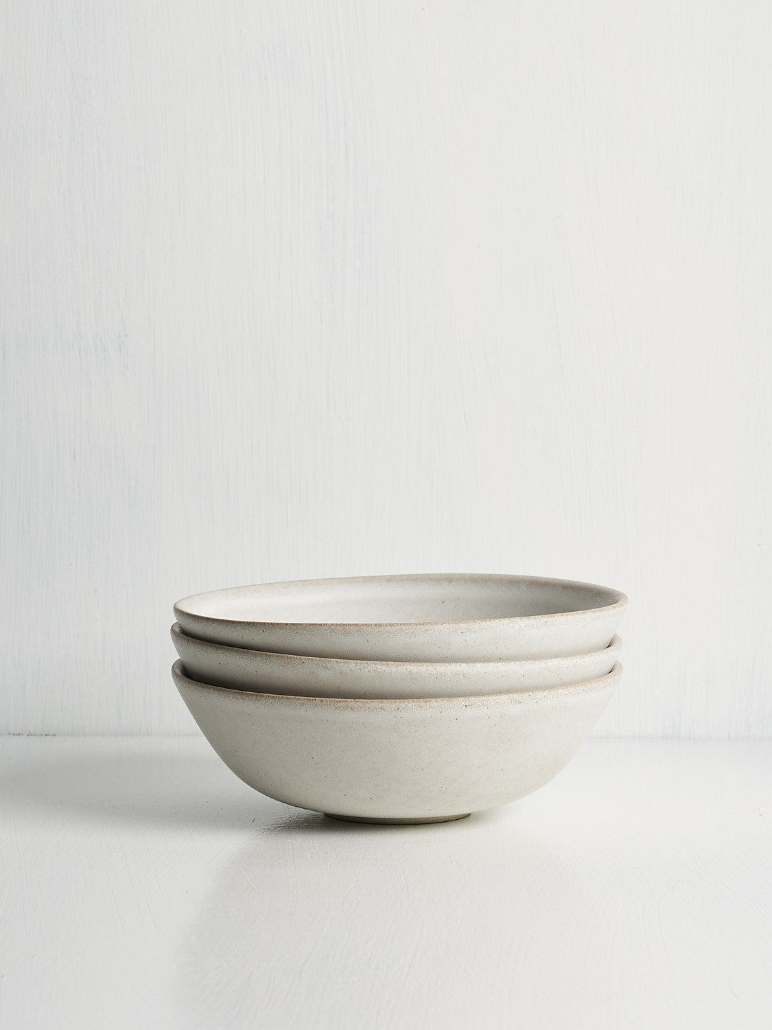 A stack of white ceramic soup or cereal bowls on a white backdrop