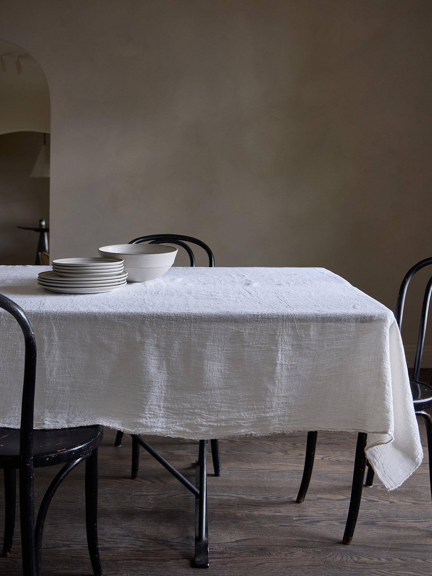 Dining table with a white linen tablecloth and black chairs against a Roman clay wall.