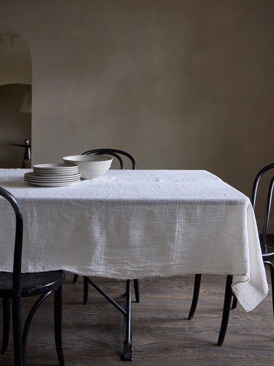 Dining table with a white linen tablecloth and black chairs against a Roman clay wall.
